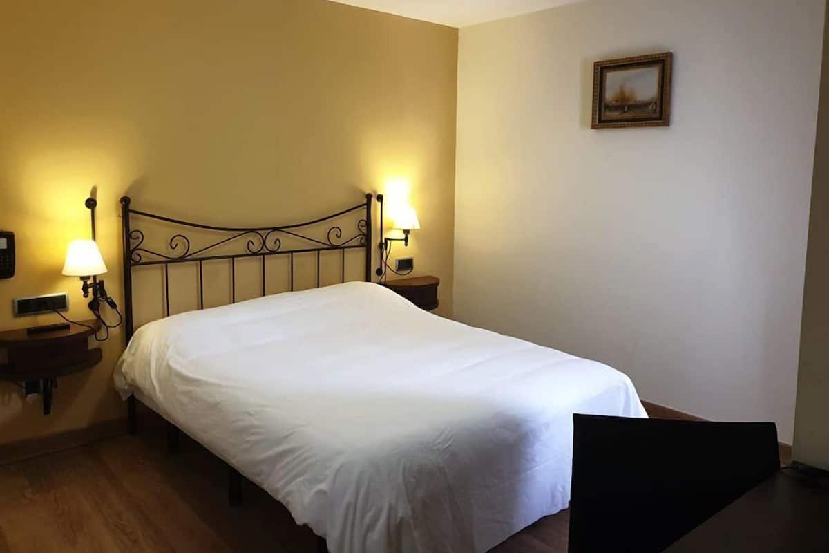 A hotel room with a single bed, two bedside tables, a nightstand, a wall-mounted lamp, and a framed picture on the wall.