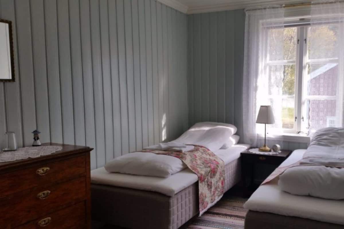 Quarto com duas camas, um penteoudeiro, uma janela com cortinas e uma luminária em uma mesa de cabeceira.