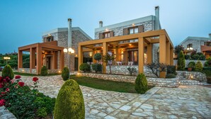A modern hotel with stone and wood exterior, multiple balconies, and a well-maintained garden. - Enastron Villas (Trifylia)