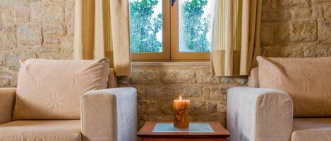 A cozy room with a stone wall, two beige sofas, a glass coffee table, and a lit candle on a tray.