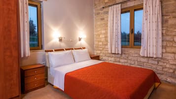 Un dormitorio con cabecera de madera, colcha roja, dos mesitas de noche y una pared de piedra.
