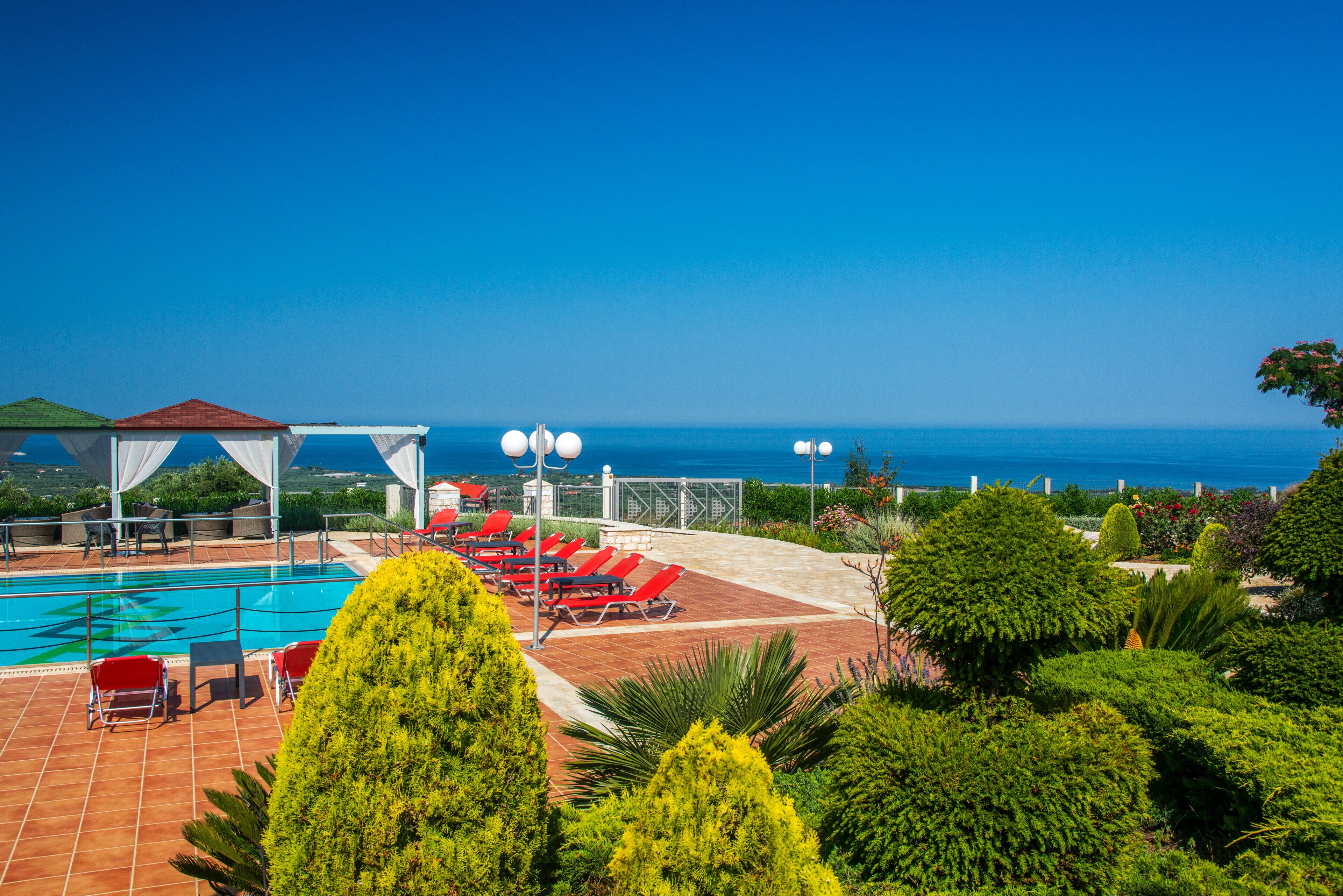 A rooftop pool area with red lounge chairs and a view of the sea.