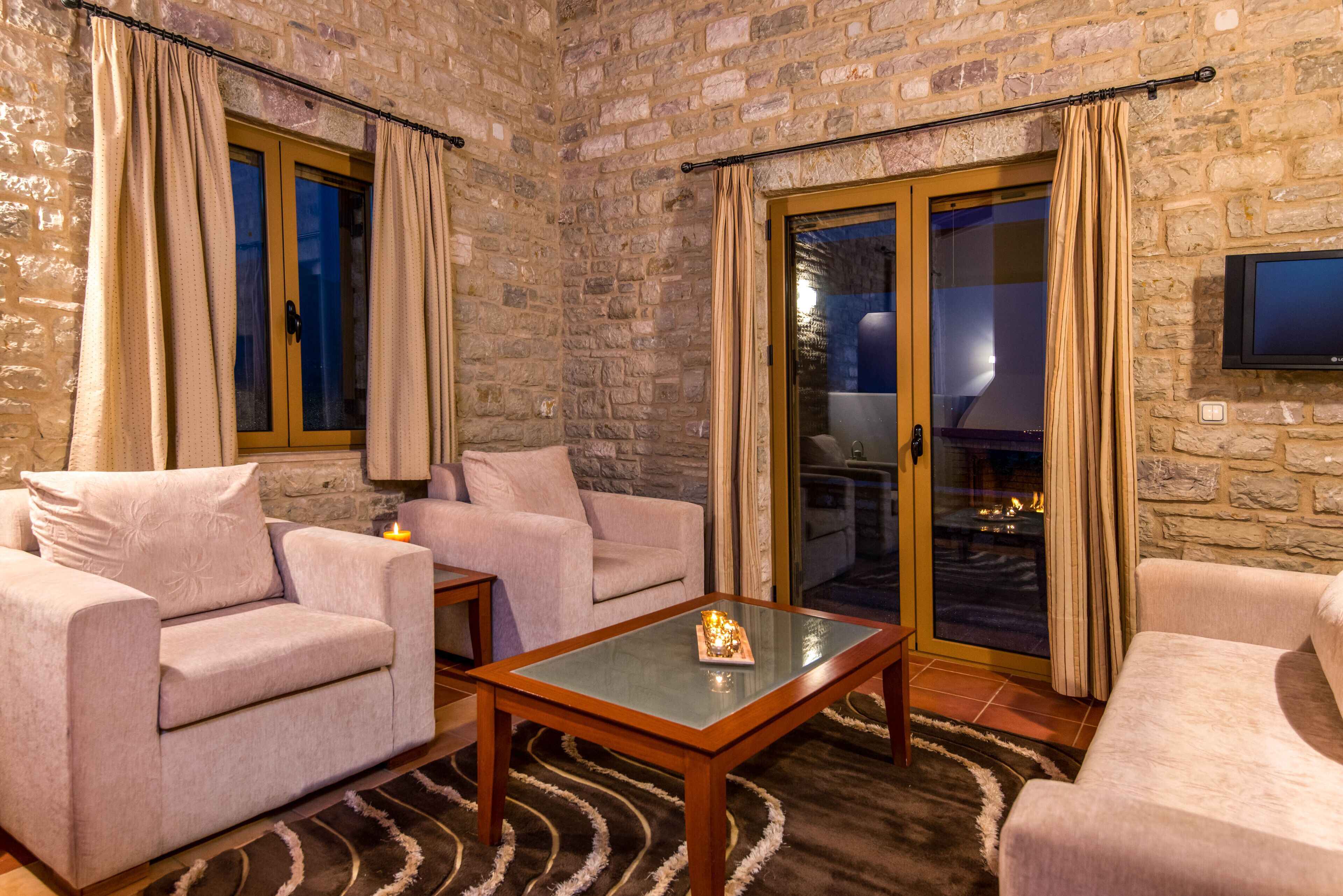 A cozy living room with a stone wall, two sofas, a glass coffee table, and a sliding glass door leading to a balcony.