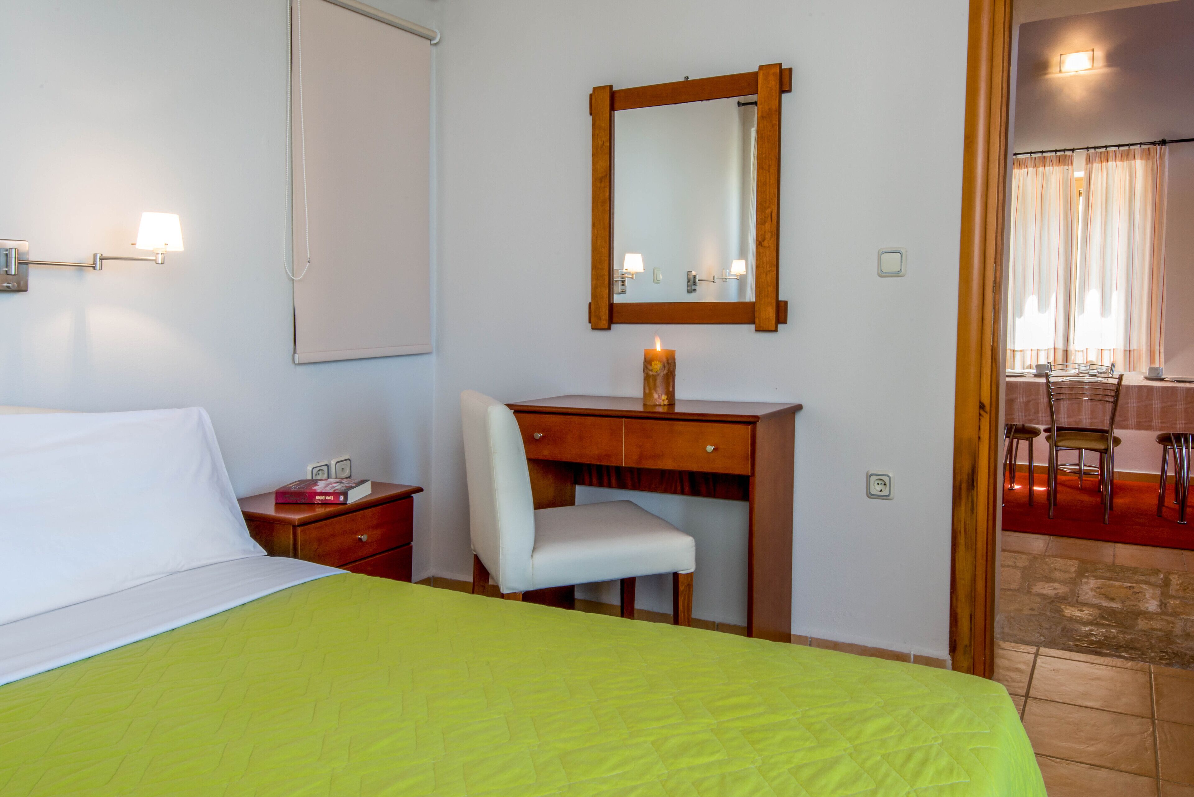Habitación de hotel con cama, escritorio, silla, espejo y una vela encendida.
