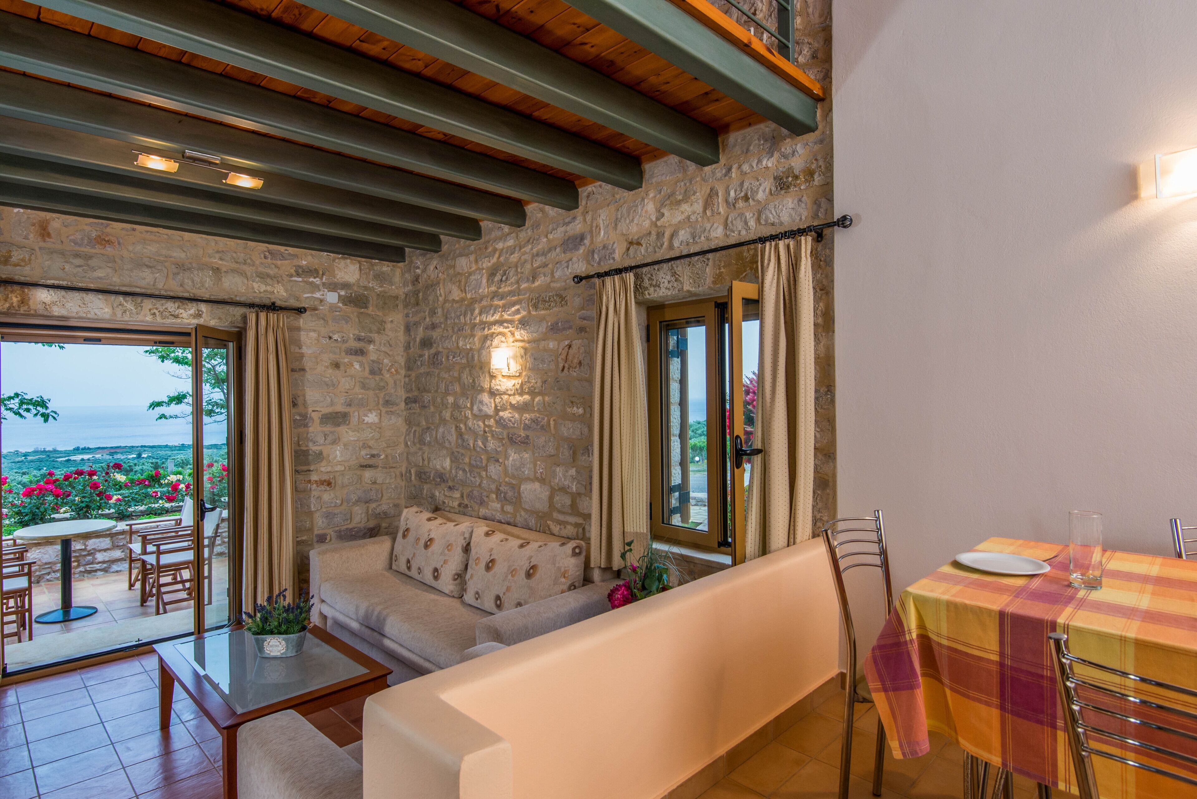 Une pièce chaleureuse avec des murs en pierre, un canapé, une table à manger avec des chaises et une vue sur un jardin.