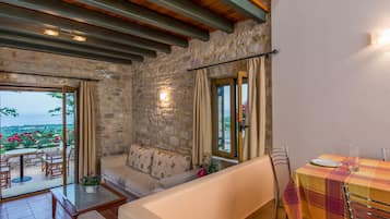 Une pièce chaleureuse avec des murs en pierre, un canapé, une table à manger avec des chaises et une vue sur un jardin.