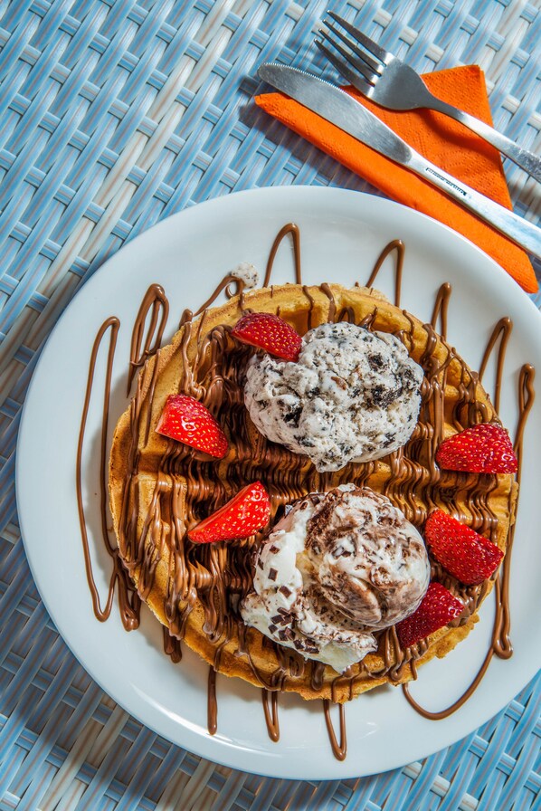 A plate of waffles with chocolate drizzle and strawberries, accompanied by a fork and knife on an orange napkin.