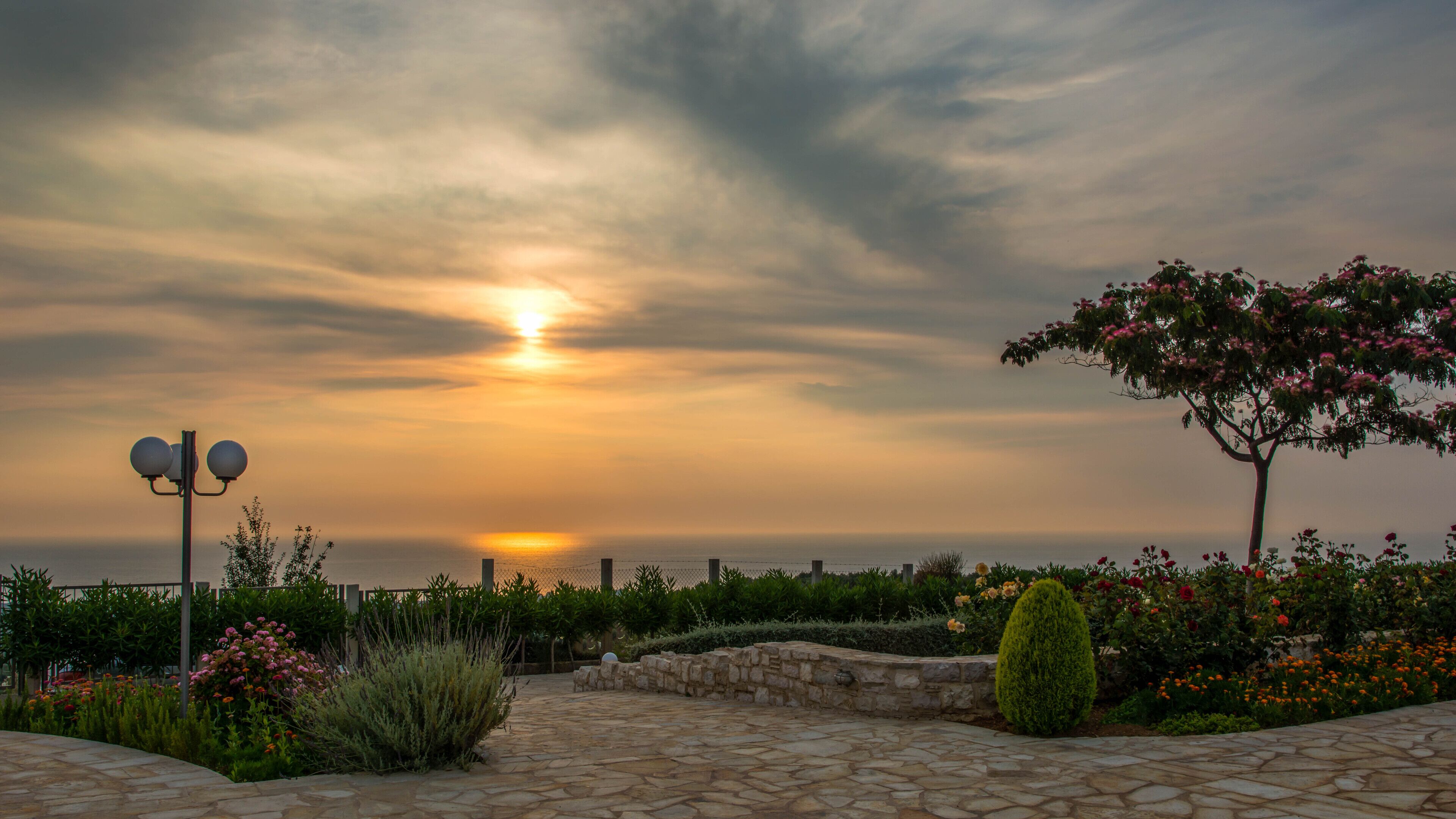 A stone pathway leading to a garden with a sunset view.