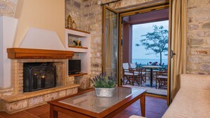 A cozy living area with a fireplace, a table with a potted plant, and a view of the outdoors through a glass door. - Enastron Villas (Trifylia)