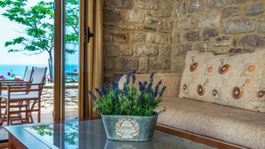 A room with a stone wall, a sofa with patterned cushions, and a table with a glass top. - Enastron Villas (Trifylia)