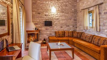 A cozy living room with a stone wall, a fireplace, a sofa, a coffee table, and a laptop on a wooden table.