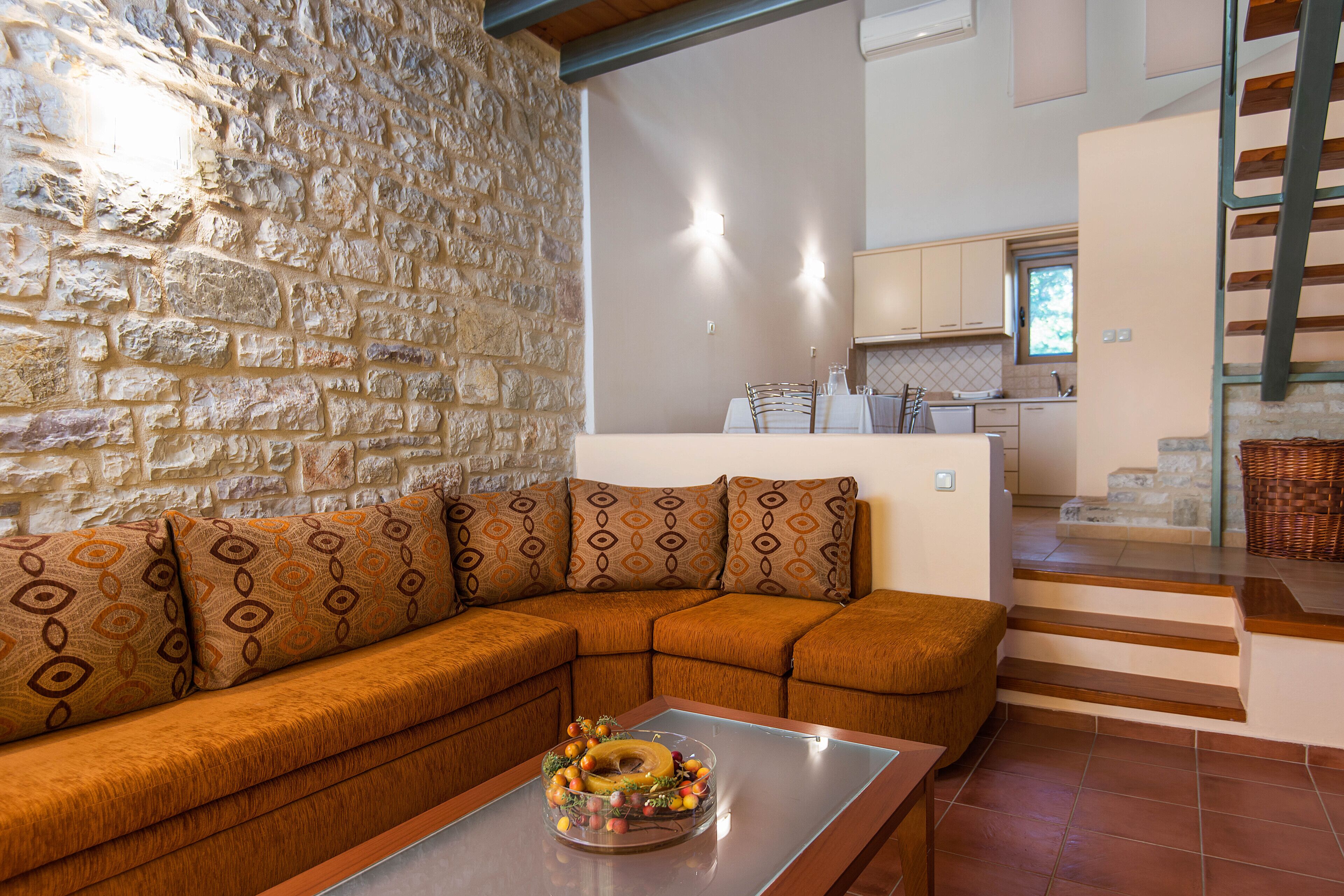 A living room with a stone wall, a brown sectional sofa, and a glass coffee table with a fruit centerpiece.