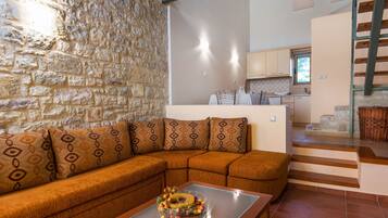 A living room with a stone wall, a brown sectional sofa, and a glass coffee table with a fruit centerpiece.