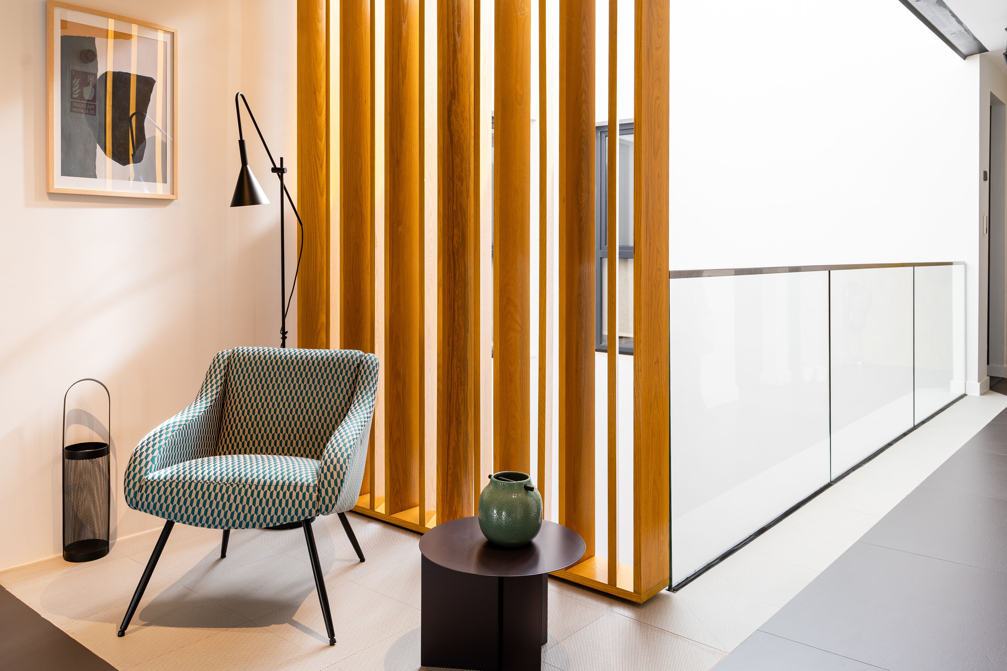 Un interior moderno con un sillón estampado, una mesita redonda con un jarrón y un divisor alto y estrecho con listones verticales.