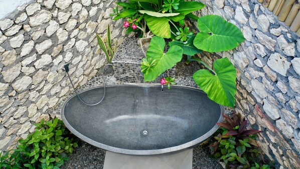 A freestanding black water feature with a spout, surrounded by a stone wall and various plants. - Jungle Paradise (Penida Island)