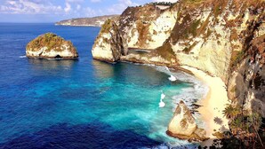 A coastal landscape with clear blue waters, rocky cliffs, and a sandy beach. - Jungle Paradise (Penida Island)