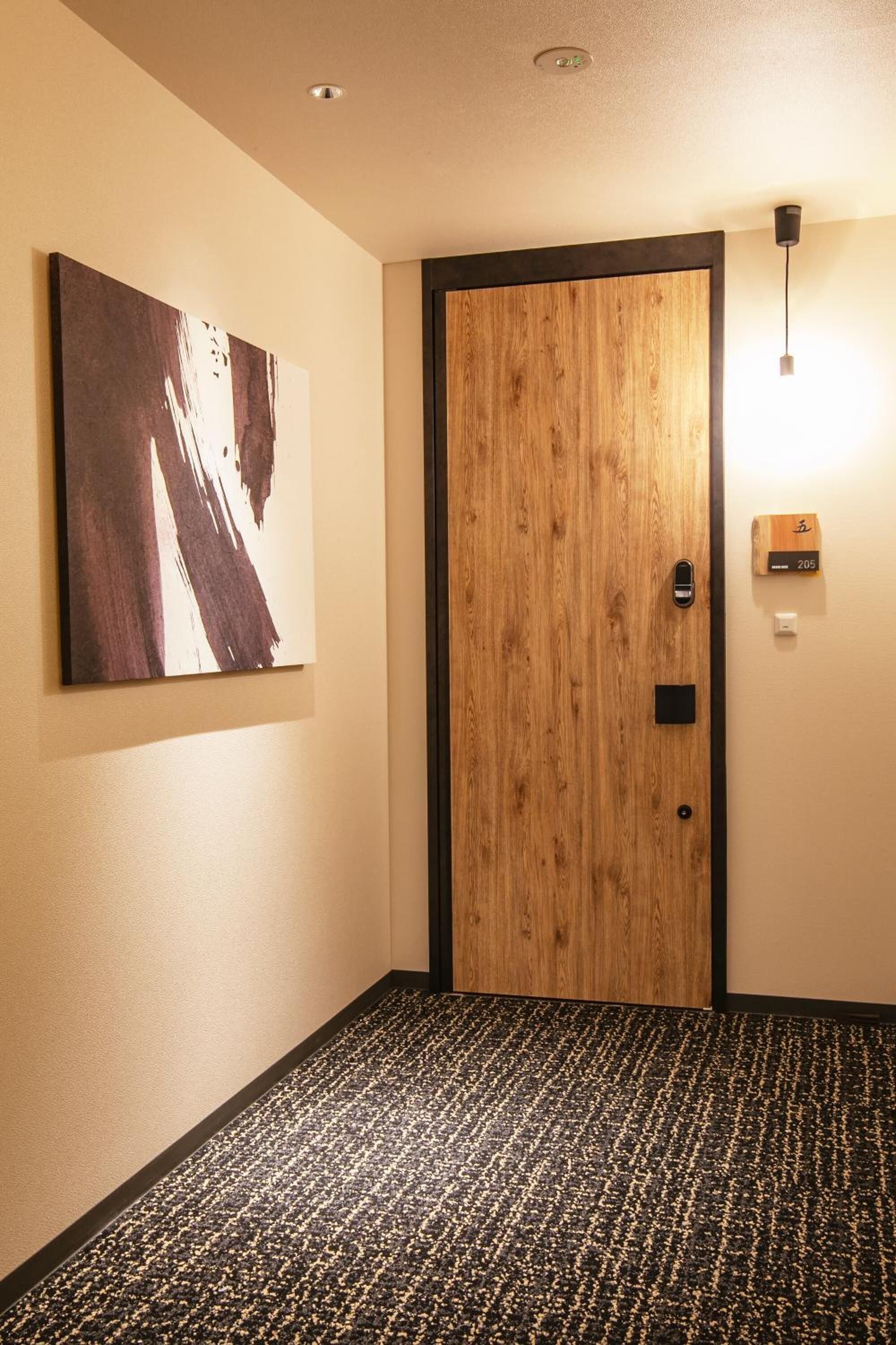 A hotel room with a wooden door, a wall-mounted light, and a carpeted floor.