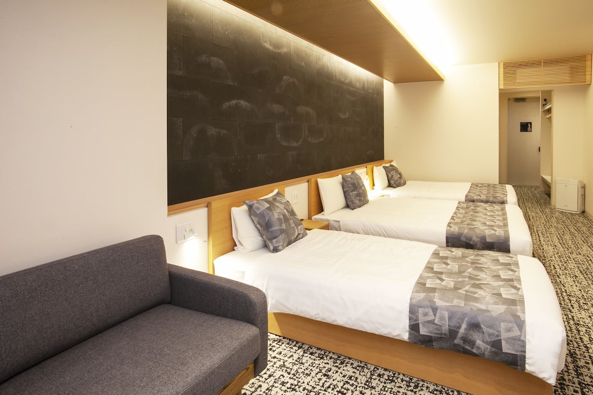 A hotel room with two beds, a gray sofa, and a patterned rug.