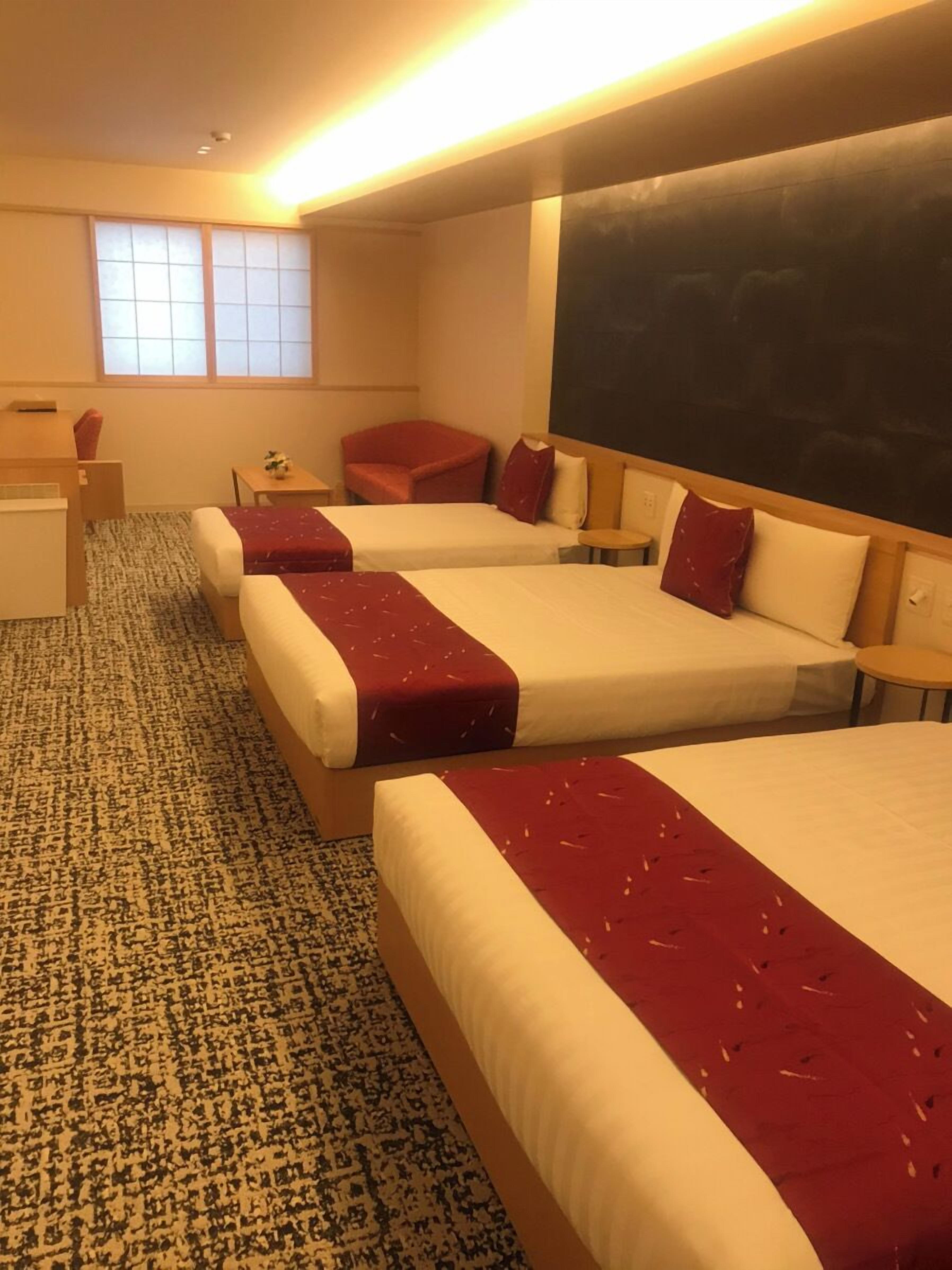 Habitación de hotel con tres camas, un escritorio, una silla y una mesita.