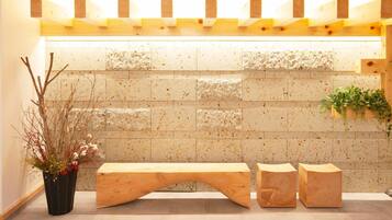 A reception area with a wooden bench, a potted plant, and a wall with a unique texture.