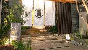 A modern hotel entrance with a traditional Japanese gate, a stone pathway, and a well-lit facade. - GRAND BASE Osu (Nagoya)