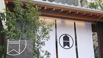 A hotel entrance with a modern facade, a sign indicating 'Hotel Grand Base OSU', and a covered walkway with a pergola.