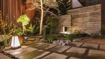A well-maintained garden with stone pathways, a variety of plants, and a modern building with a wooden facade.