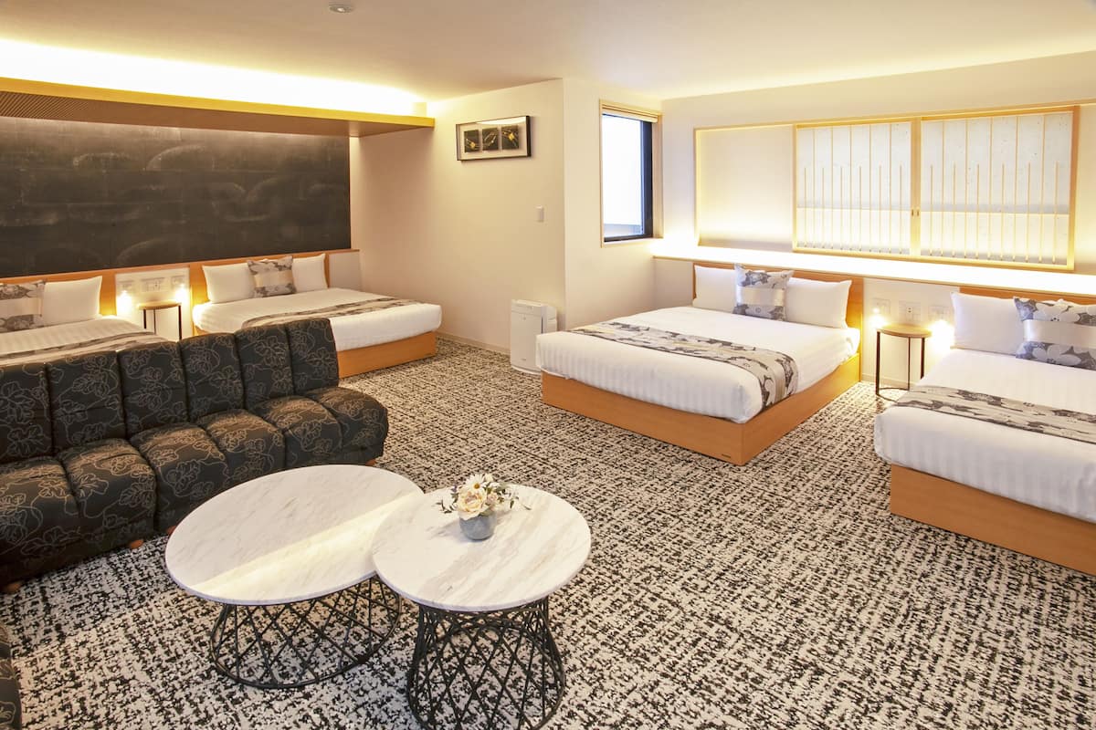 A hotel room with two beds, a sofa, two round tables, a TV, and a large window.