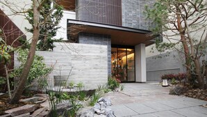 A modern house with a stone pathway, a wooden fence, and a variety of plants. - GRAND BASE Osu (Nagoya)