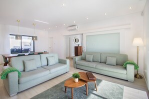 A modern living room with two light grey sofas, a wooden coffee table, and a dining area with a wooden table and chairs.