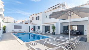 Zona de piscina al terrat amb gandules, taula i ombrelles.