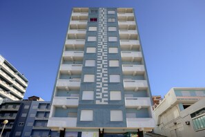 Korkea, moderni rakennus, jossa on keskeisellä paikalla sijaitseva portaikko, useita parvekkeita ja avoin, selkeä taivas.