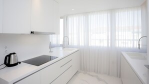 Eine moderne Küche mit weißen Schränken, einer schwarzen Induktionskochplatte und einem Wasserkocher.