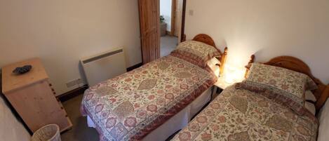 Une chambre avec deux lits, une commode en bois, un radiateur et une porte donnant sur une autre pièce.