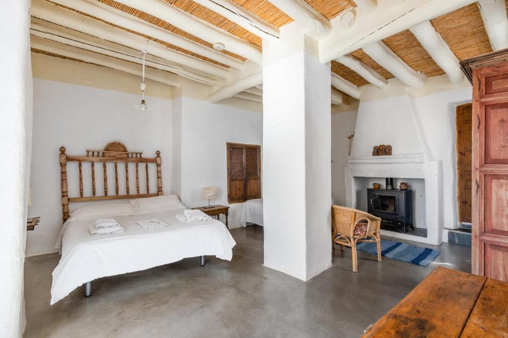 Un dormitorio con cama, cabecero de madera, mesita de noche, sillón, chimenea y mesa de madera.