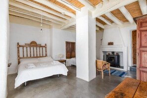 A bedroom with a bed, a wooden headboard, a nightstand, a chair, a fireplace, and a wooden table. - Las Chimeneas (Nevada)