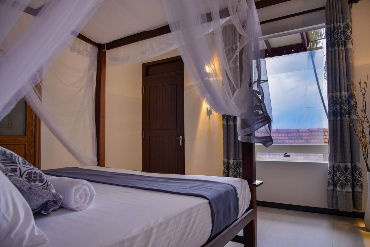 Une chambre à coucher avec un lit, une porte en bois, une fenêtre avec des rideaux et un balcon offrant une vue.
