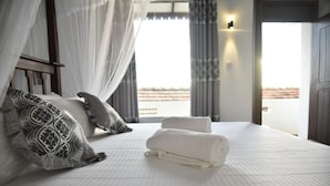 A neatly made bed with a white bedspread and two pillows, a rolled-up towel, and a window with curtains. - Wagon Wheel Inn - Hostel (Boossa)