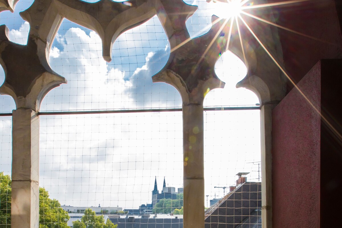 A Gothic-style window with a view of a cityscape, including a church spire.