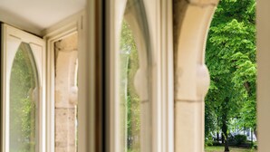 Blick durch ein Fenster mit Bogenförmigem Rahmen, das einen Park mit Bäumen und einem Weg zeigt.