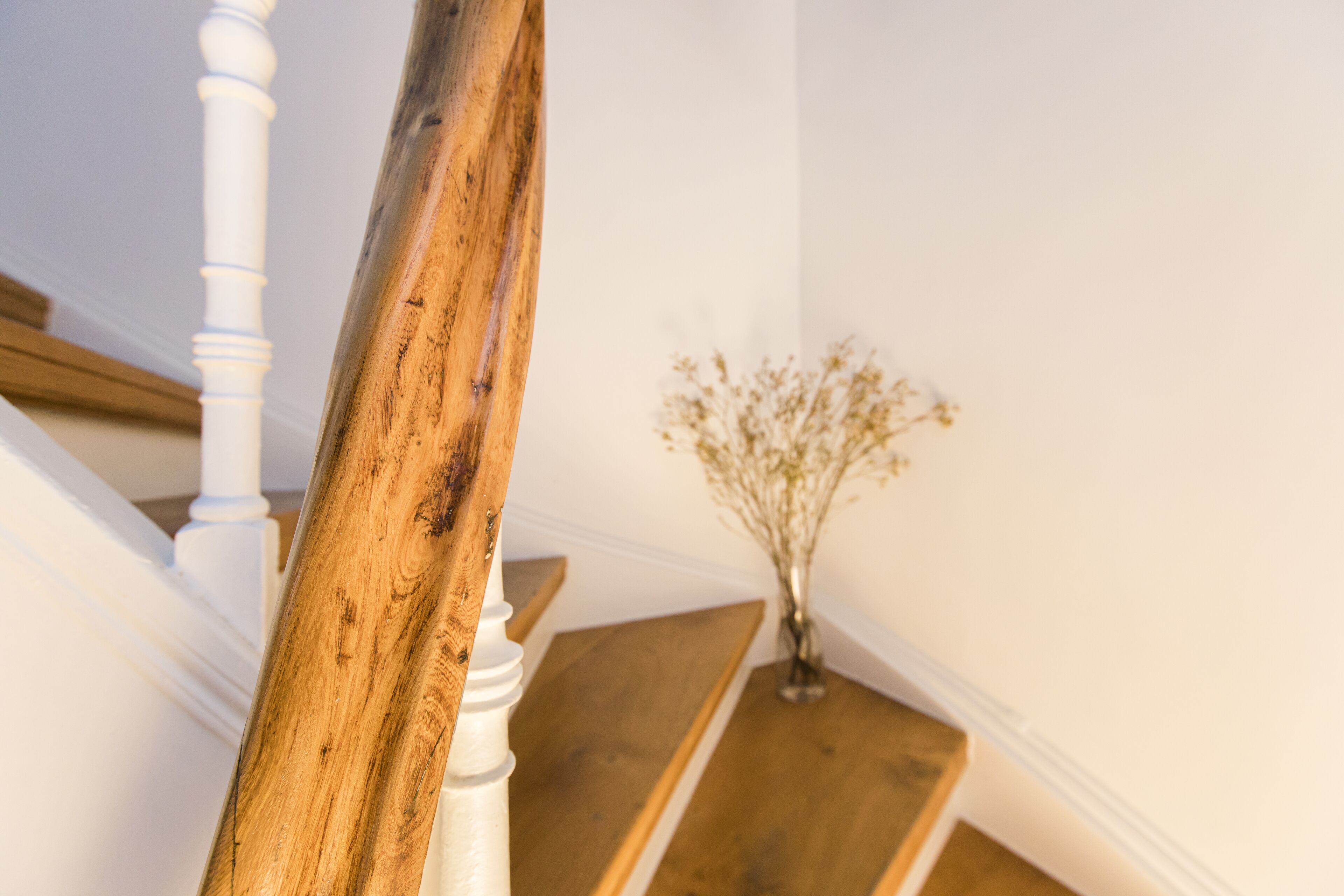 Eine Holztreppe mit weißen Wangen und einer Vase mit Trockenblumen auf der Zwischenebene.