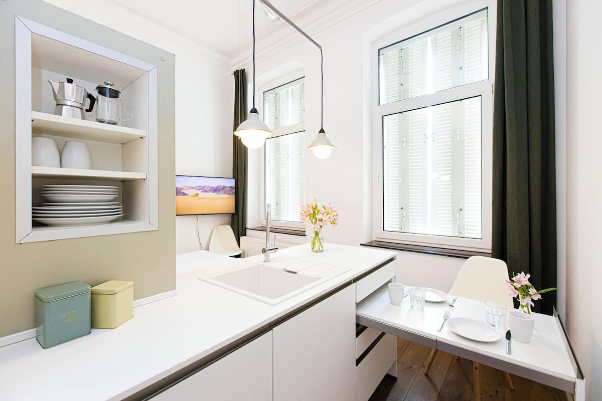 Une cuisine moderne avec des meubles blancs, un évier encastré et un coin repas avec une table mise pour deux personnes.