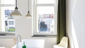 Eine moderne Küche mit einer weißen Spüle, zwei Pendelleuchten und Blick auf die Stadt durch große Fenster.