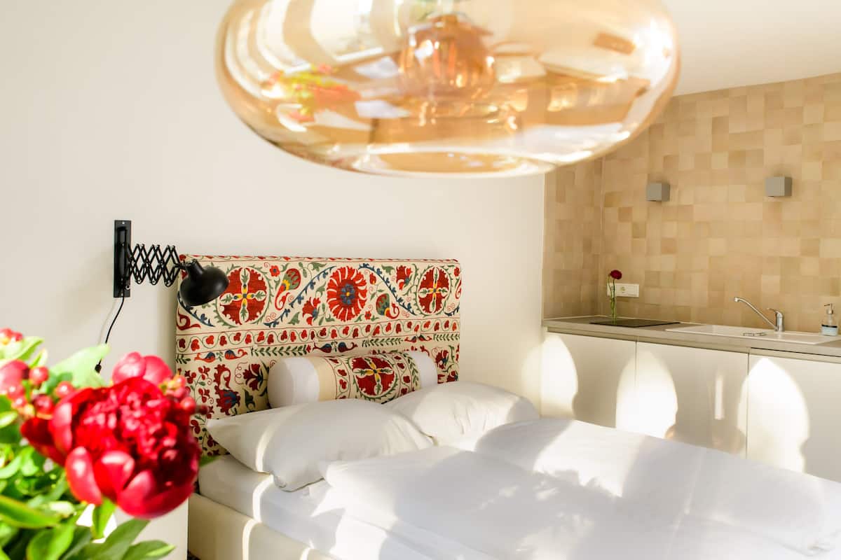Une chambre d’hôtel comprenant un lit, une tête de lit décorative, un petit coin cuisine et une plante en pot.