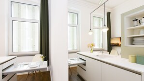 Eine moderne Küche mit weißen Schränken, ein Essbereich mit Tisch für zwei Personen und ein Fenster mit Jalousien.