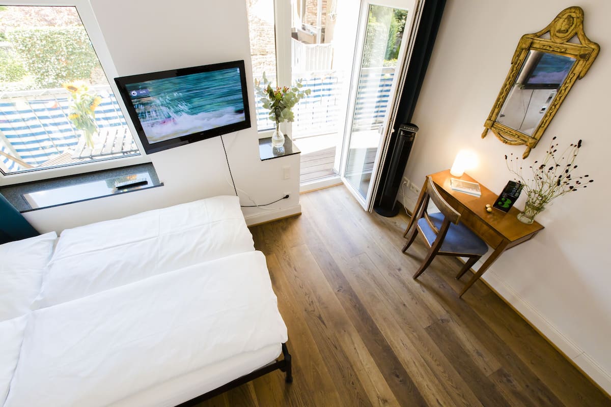 Une chambre à coucher avec un lit, un téléviseur fixé au mur, une petite table avec une lampe et une fenêtre donnant sur l’extérieur.