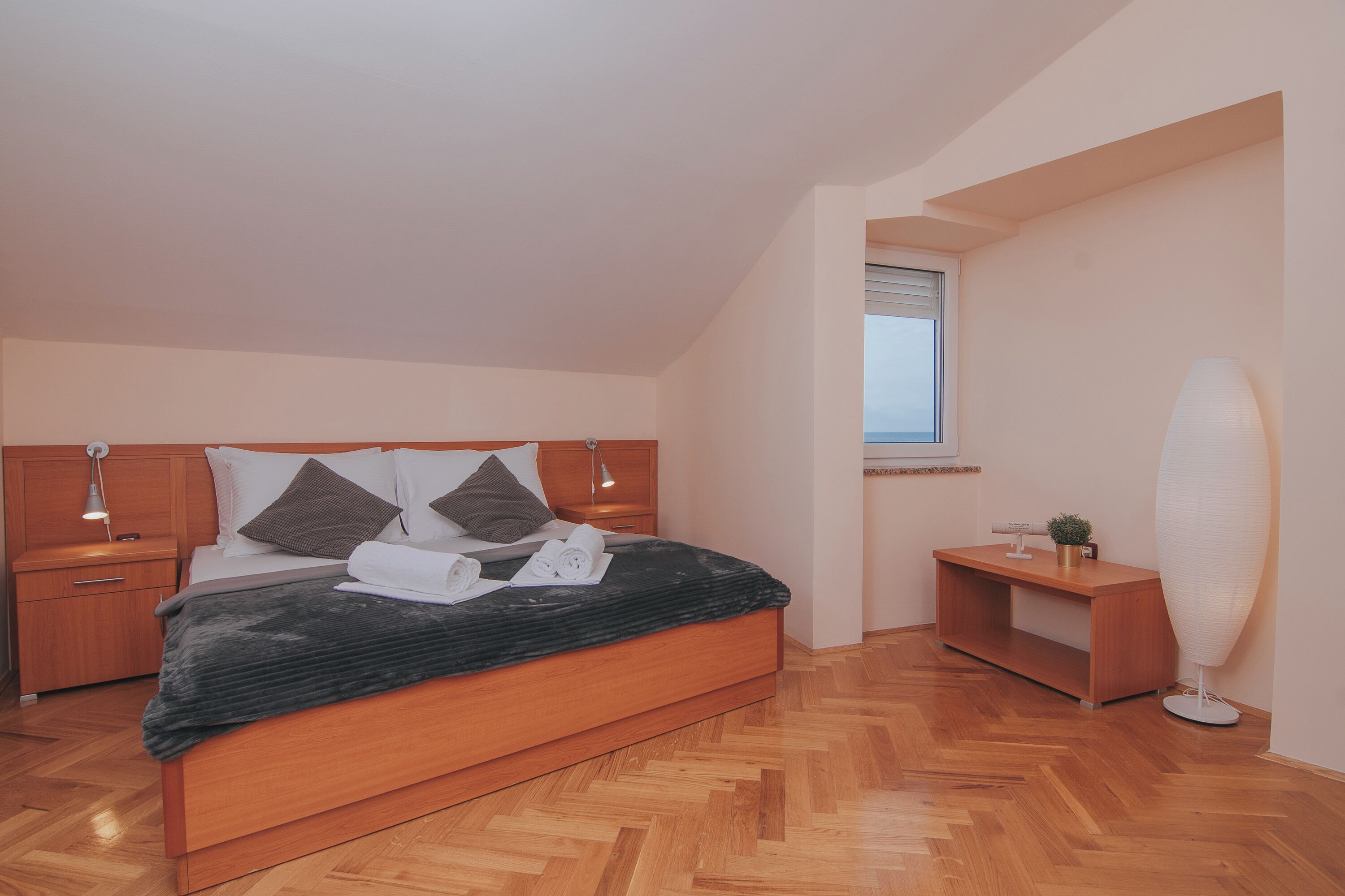 A bedroom with a wooden bed, bedside tables, a nightstand, a desk, and a floor lamp.
