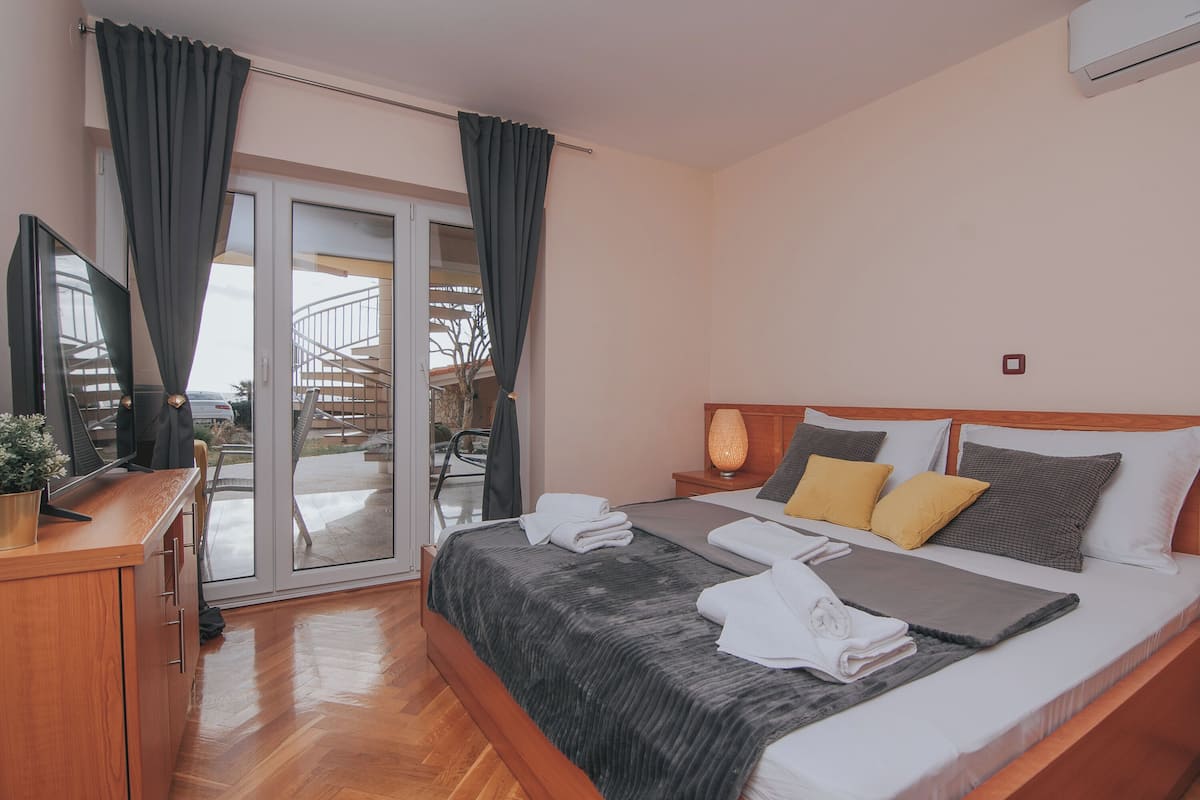 Habitación de hotel con cama, escritorio, televisor y puerta corrediza de vidrio que da a un balcón.
