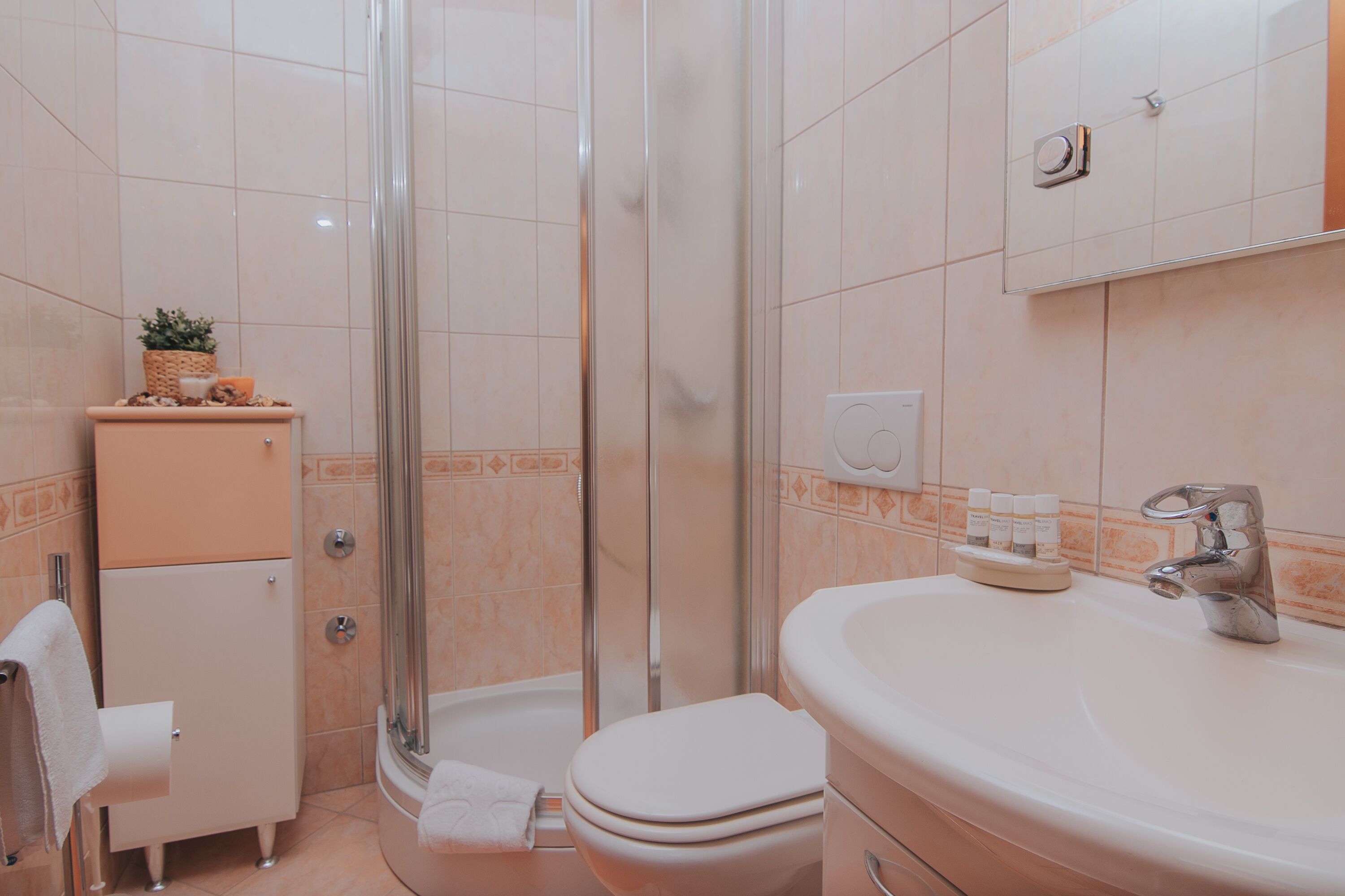 A bathroom with a shower, toilet, sink, and a small cabinet with toiletries.