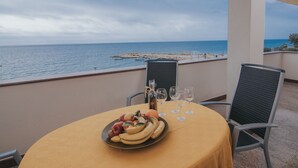 Une table avec un assortiment de fruits, des verres à vin et une bouteille, le tout placé sur un balcon donnant sur la mer.
